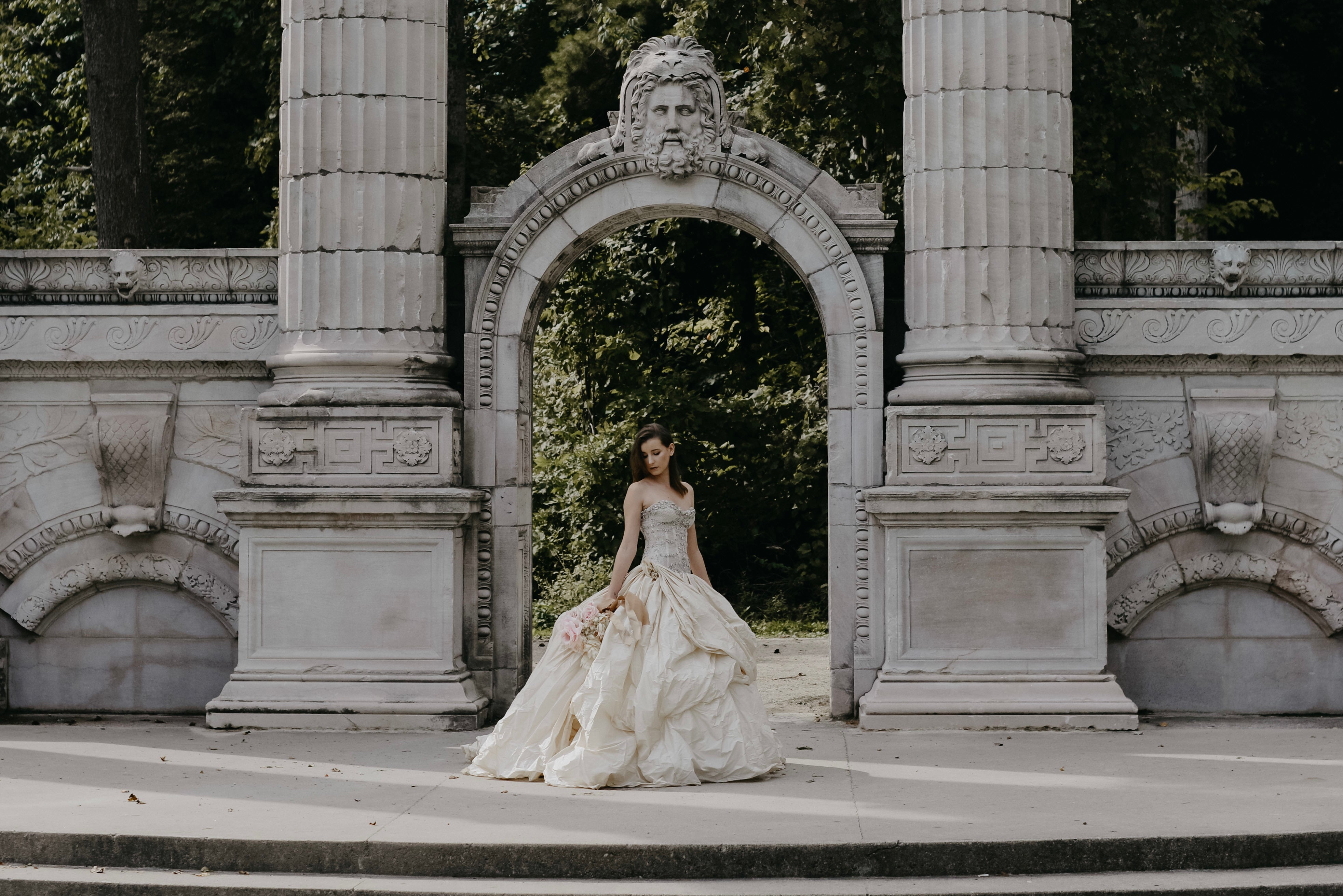 womean wearing white wedding dress under large concrete pillars.