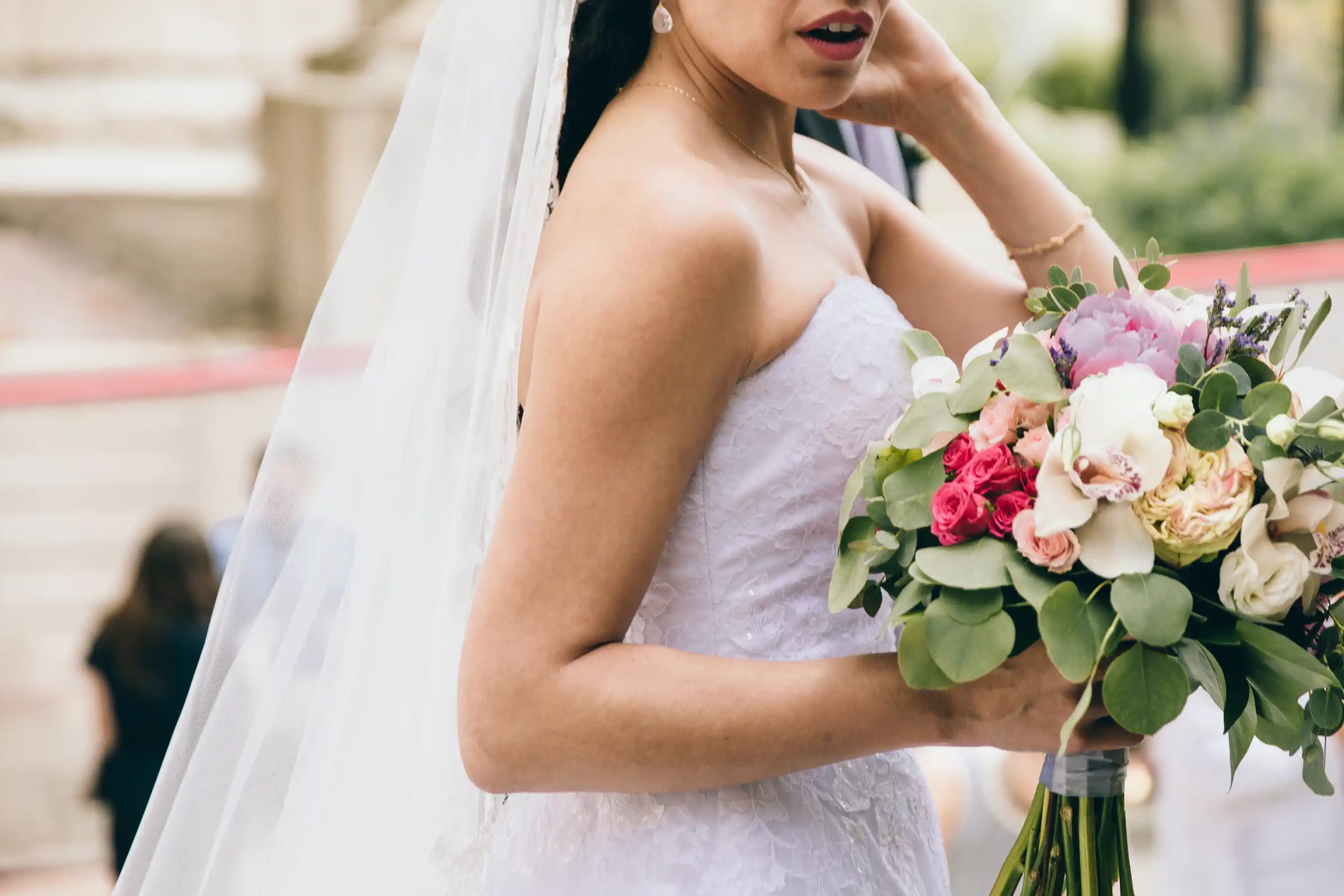Bride wearing strapless lace wedding dress with veil holding pink and white bridal bouquet