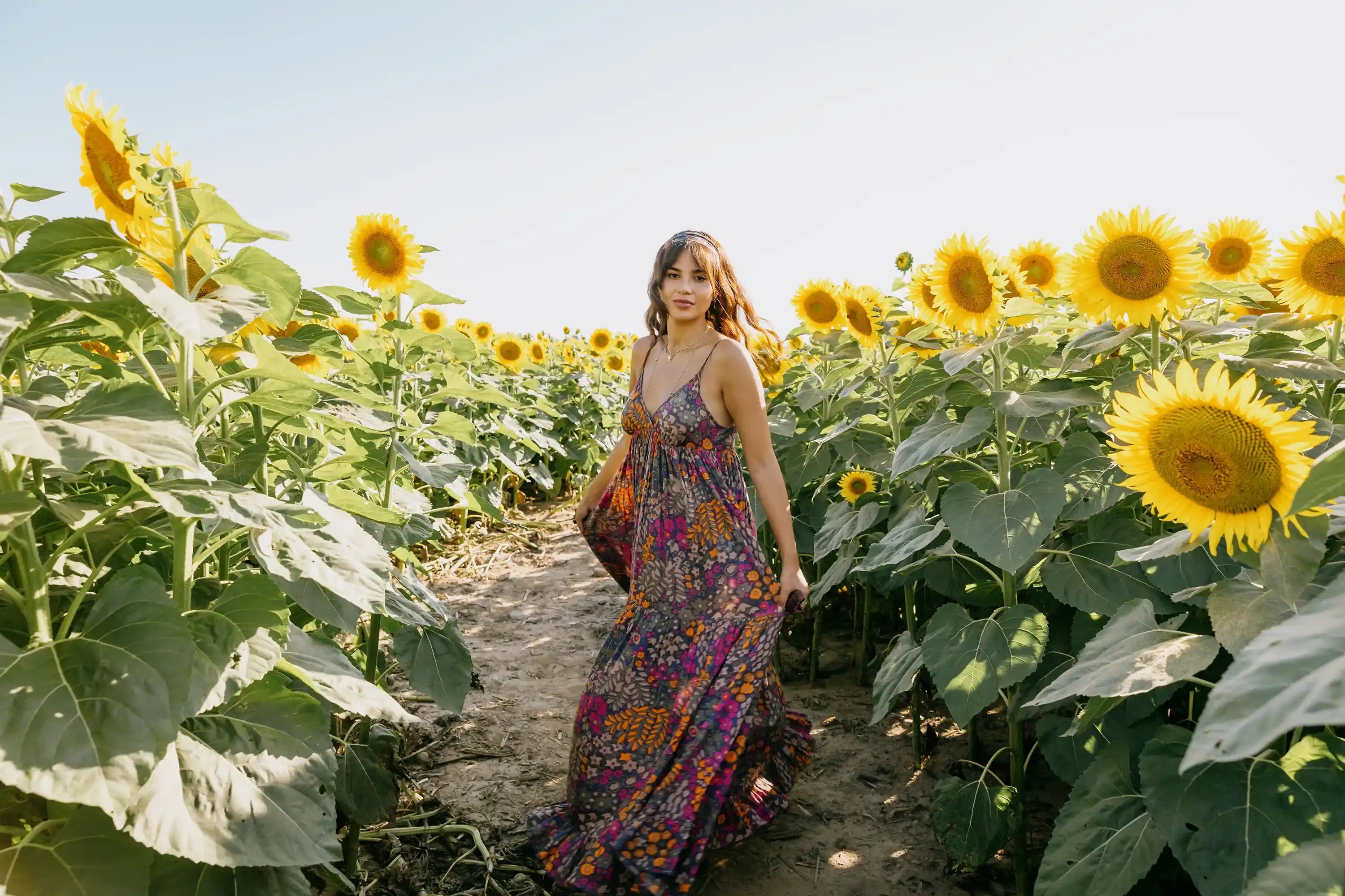 Woman wearing floral boho maxi mother of the bride dress with spaghetti straps standing in sunflower field