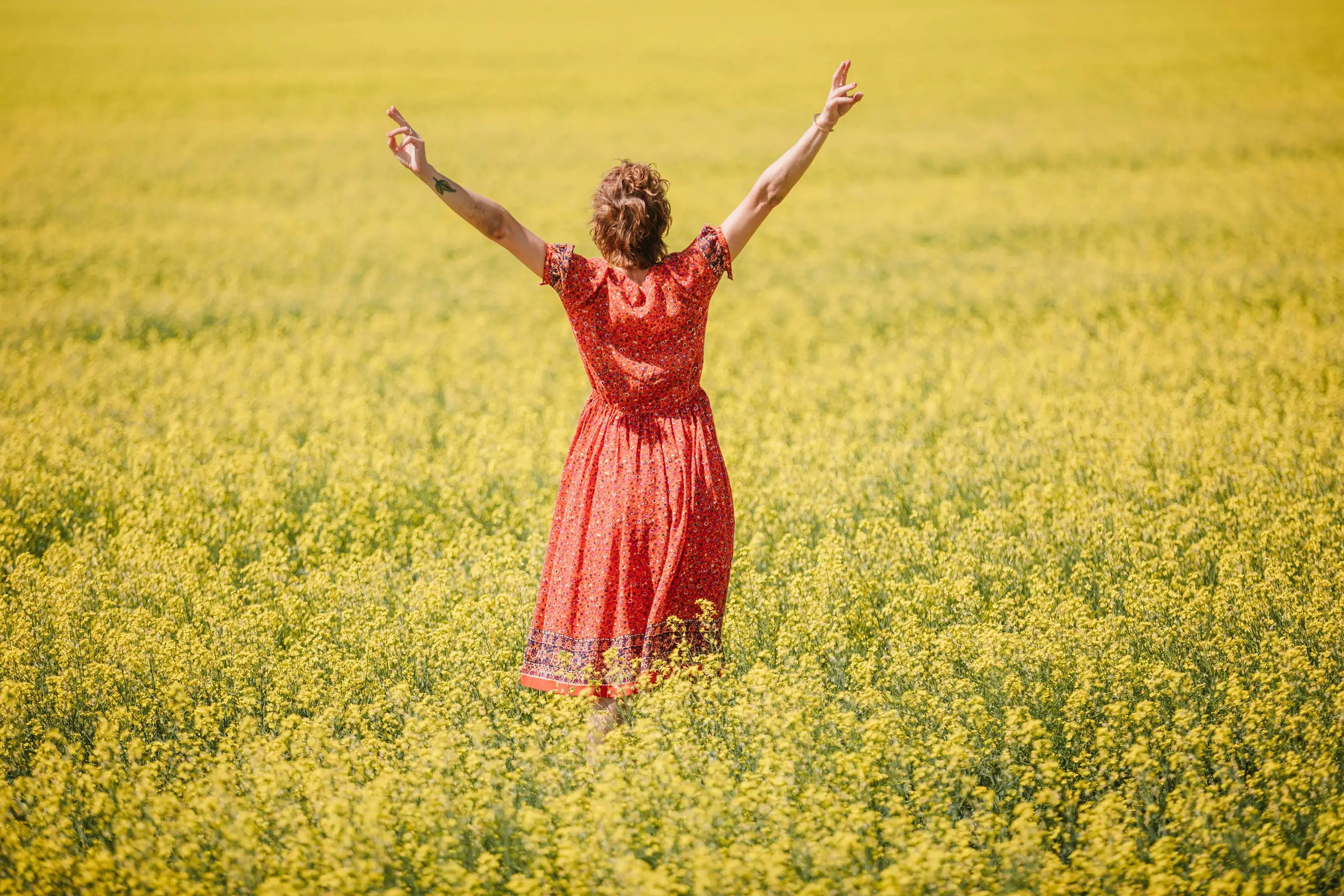 Woman wearing red floral midi mother of the bride dress with short sleeves standing in yellow flower field